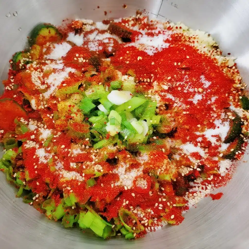 Bowl of cucumbers topped with red chili powder, scallions, garlic, and sesame seeds
