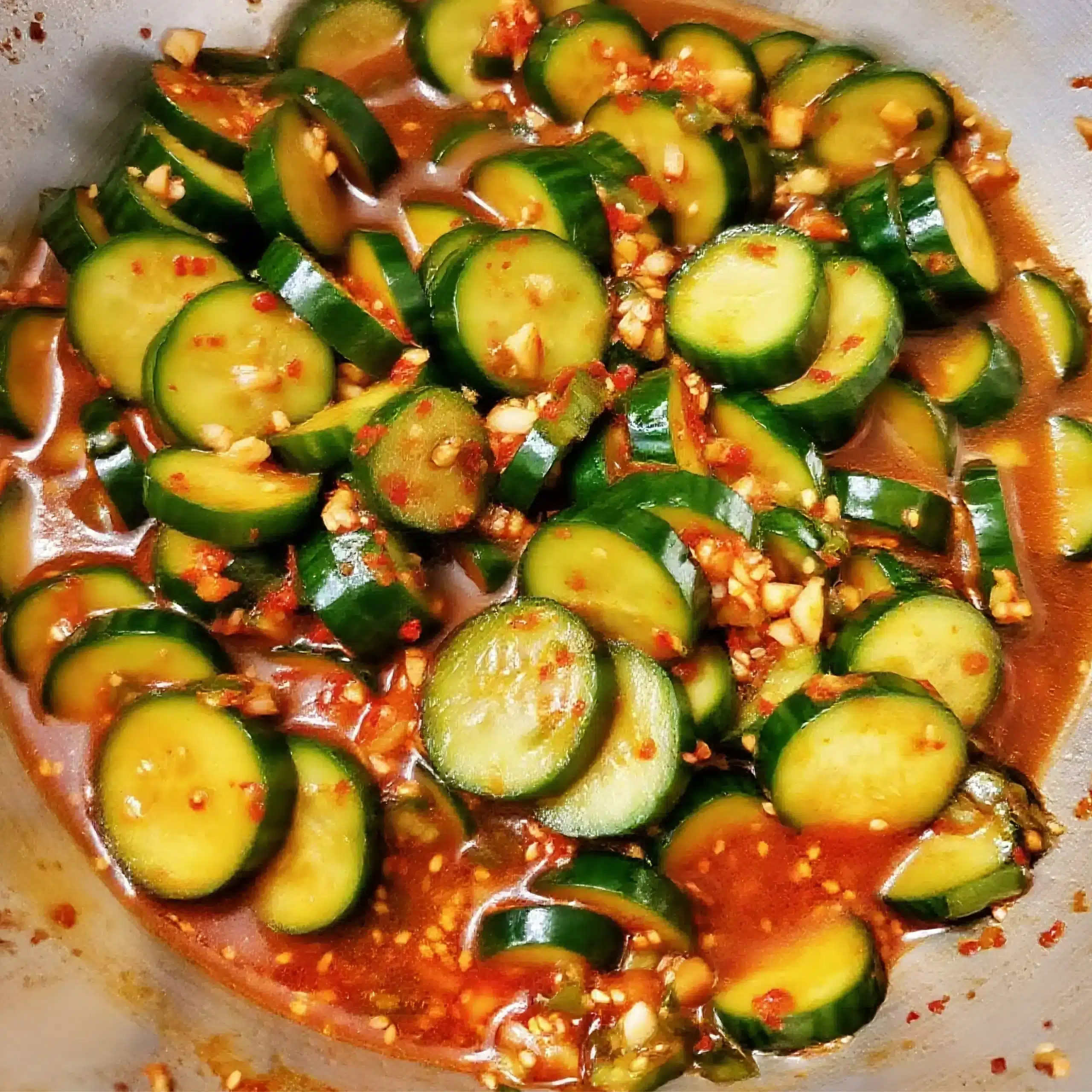 spicy Cucumber salad being mixed with red sauce, garlic, and spices in a metal bowl
