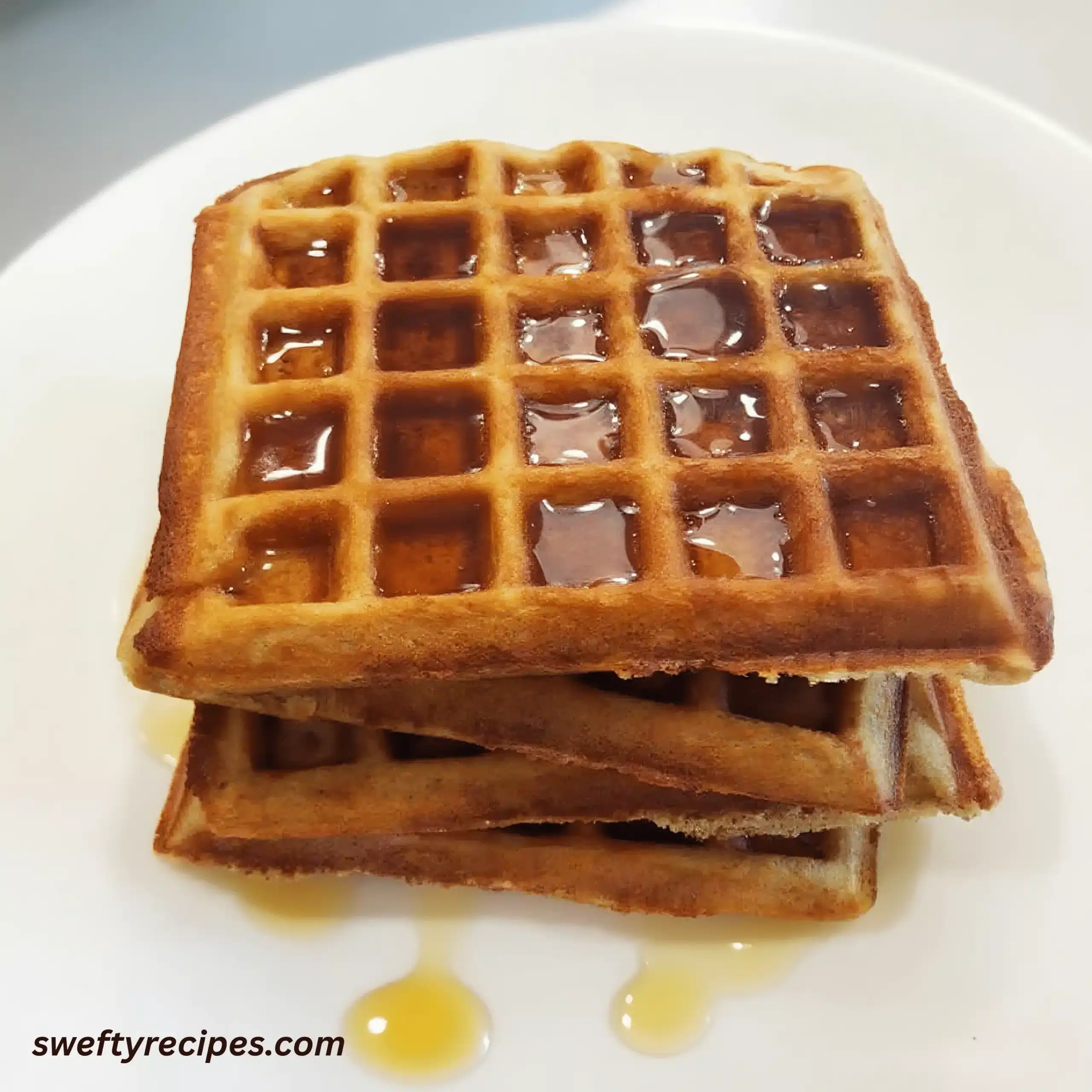 Keto Waffle Recipe 5 Golden square waffles stacked with syrup on a white plate