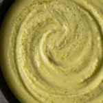 close-up of creamy pesto Alfredo sauce with a smooth swirl texture and light green color